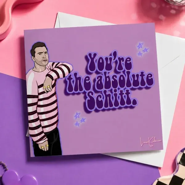 Schitt's Creek "Simply The Best" Greeting Card flat lay on colourful table.