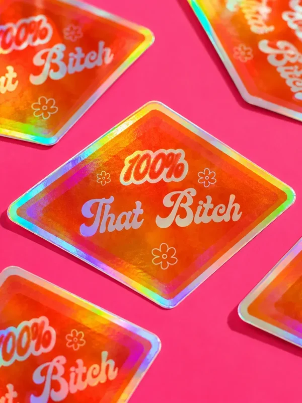 100% That Bitch Holographic Sticker on hot pink table.