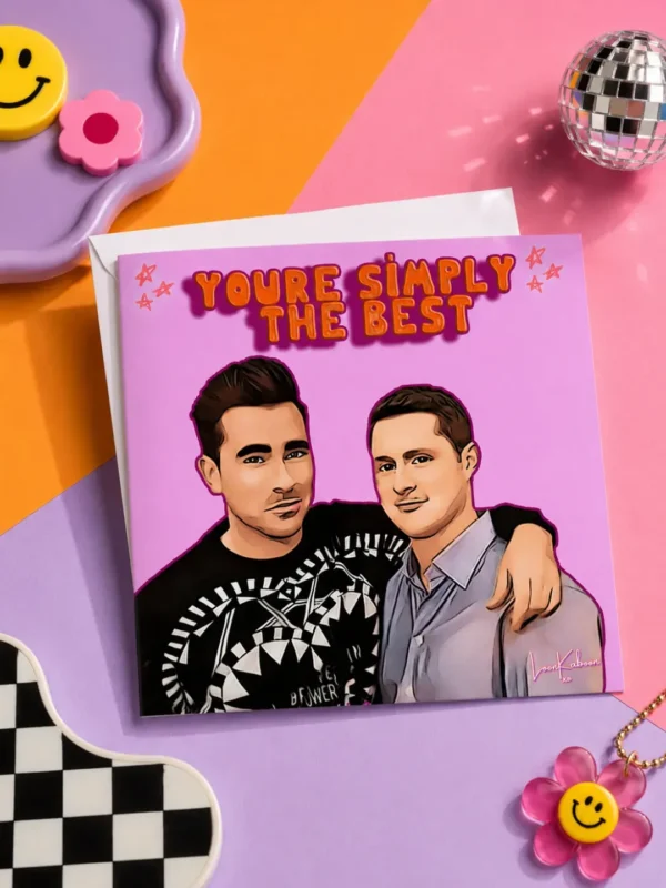 Schitt's Creek "Simply The Best" Greeting Card flat lay on funky colourful table.