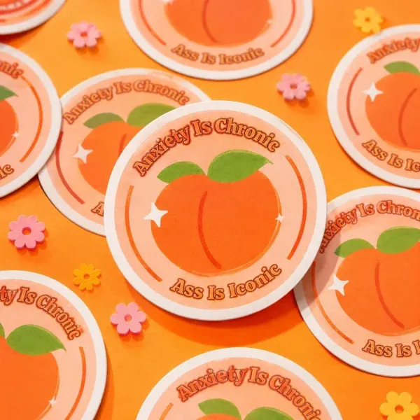Anxiety Is Chronic, Ass Is Iconic Sticker flat lay on funky orange background.
