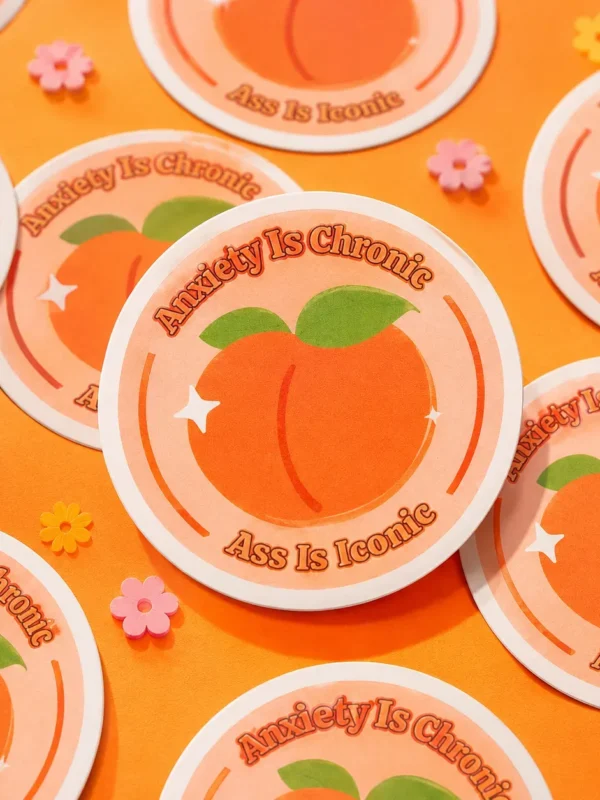 Anxiety Is Chronic, Ass Is Iconic Sticker flat lay on funky orange background.