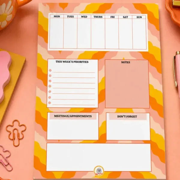 Weekly Planner A5 Notepad on a funky desk with pens, paperclips and other desk items.