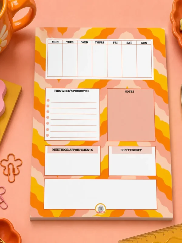 Weekly Planner A5 Notepad on a funky desk with pens, paperclips and other desk items.