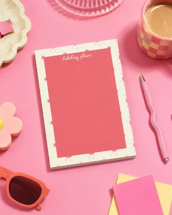 Holiday Plans A5 Notepad on a funky desk with pens, paperclips and other desk items.