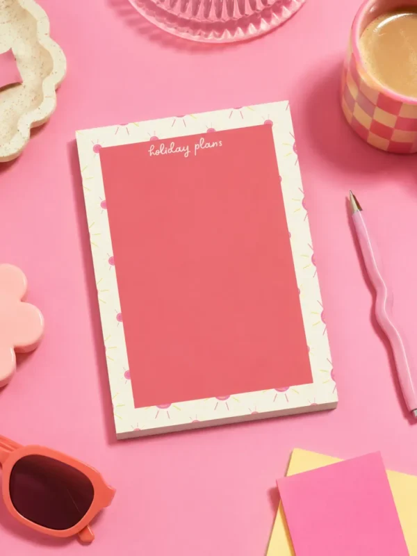 Holiday Plans A5 Notepad on a funky desk with pens, paperclips and other desk items.